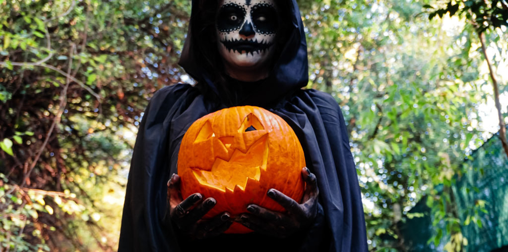 Young woman with halloween paint face mask wearing black hood LIFE